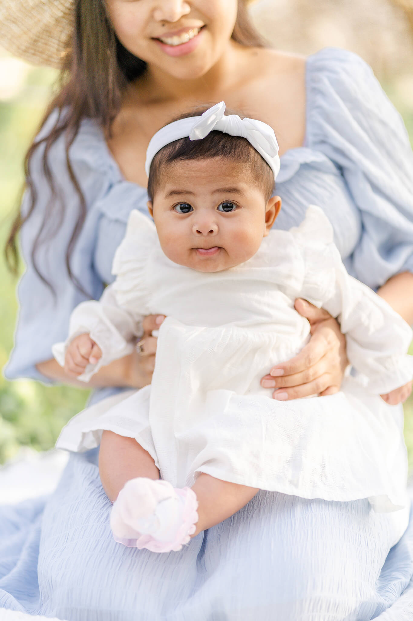 asian baby in cute white dress and headband sitting on mums laps during family photoshoot