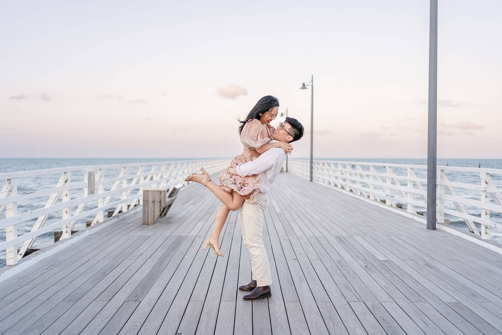 couple lifting on shorncliffe pier having engagement photos done in sandgate sunset hours.